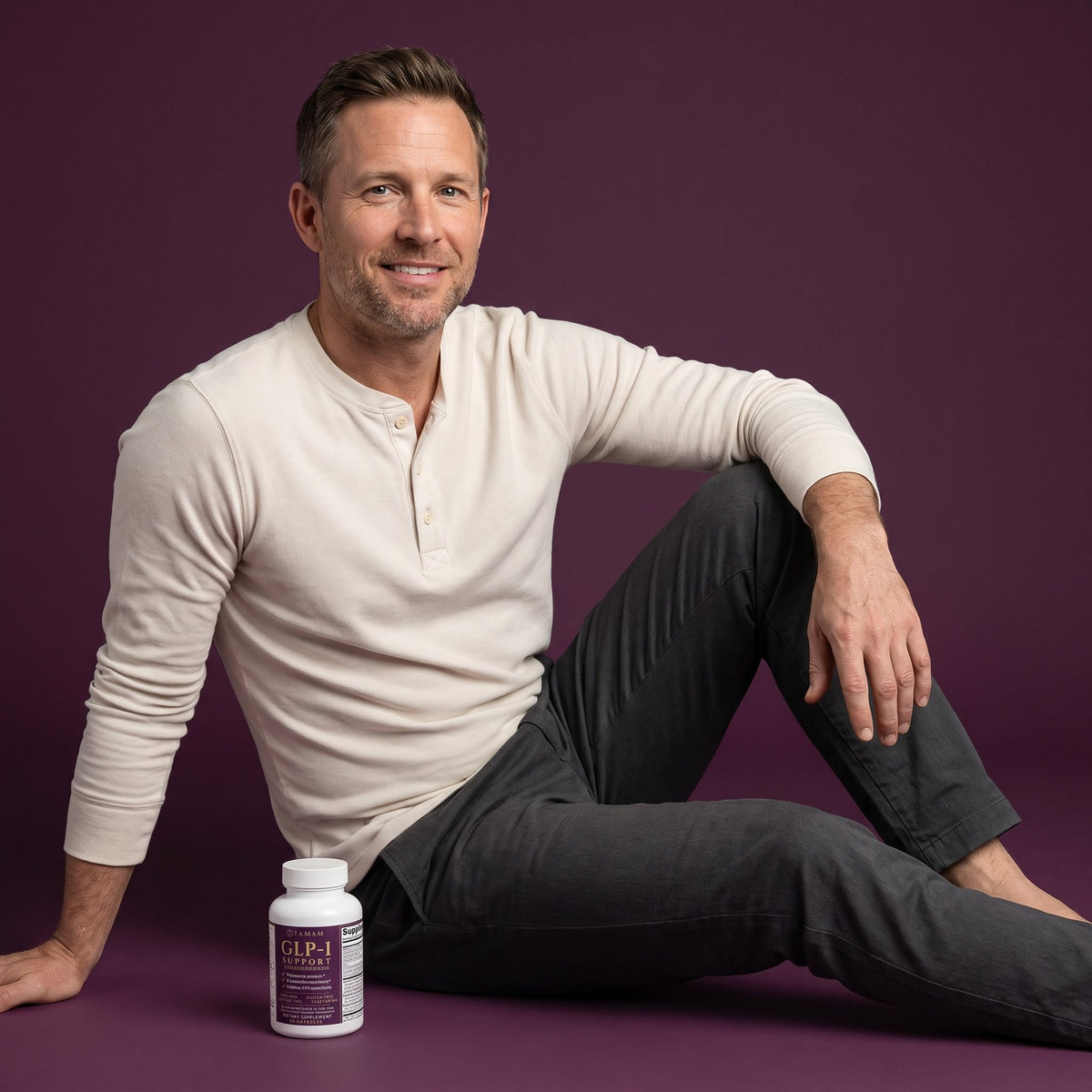 Man in a plum studio with a bottle of TAMAM