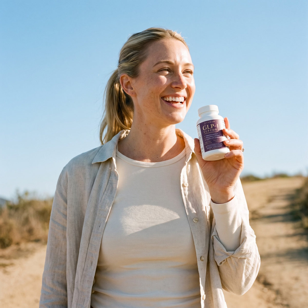 Smiling woman on a coastal path holding TAMAM